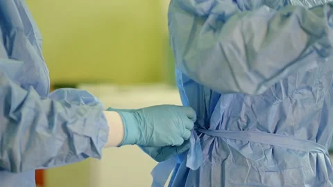 In the operating room, a doctor's assistant helps remove a surgical gown after a Video stock 235791838