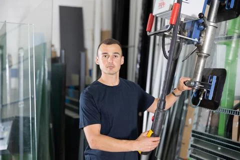 Operator maneuvering glass sheets with vacuum lifter in industrial workshop Stock Photos