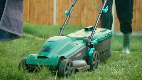 Operator pushing electric lawn mower over tall grass in rubber boots. Individual Stock Footage 314826671
