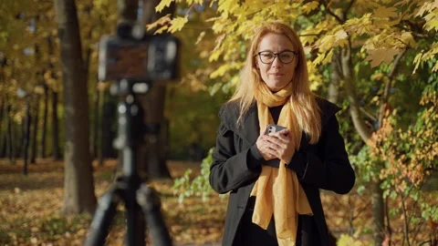 Operator records video report with red-haired woman in glasses in autumn park Video stock 163614449