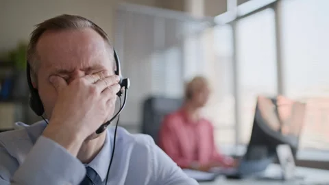 Operator Rubbing Eyes and Taking Deep Breath while Consulting Client via Headset 스톡 동영상 335751509