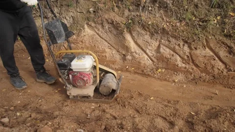 Operator uses plate compactor in trench with dust, worker operating plate Stock Footage 319582832