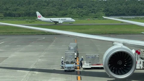 Operators unload an airplane, with an airplane taking off in the background Stock Footage 248513579