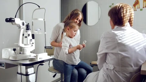 Ophthalmologist in clinic explains diagnosis about girl's eyesight - mother and Stock Footage