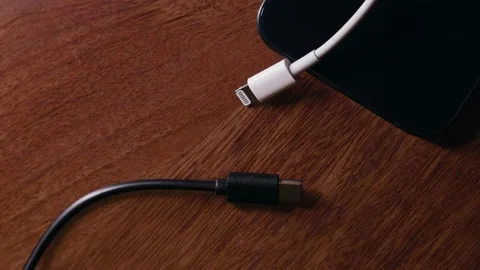 Oppossing White Apple lightning cable and black USB-C on wooden surface Stock Footage 218441412