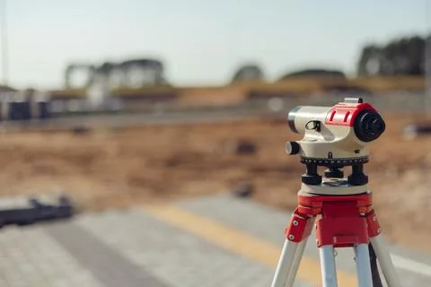Optical level is mounted on a tripod, with a construction site in the background Stock Photos