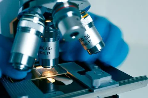 Optical microscope with gloved hands in lab Stock Photos
