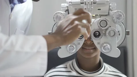 Optician doing optometry eye exam for black african american teen girl patient Stock Footage 154399394