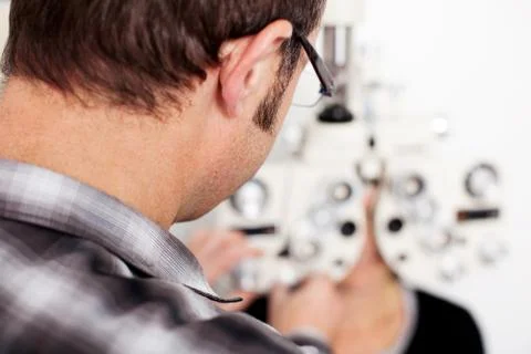 Optician examining patient's eyes in examination room Stock Photos