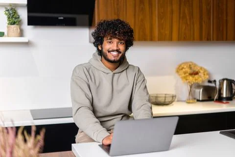 Optimistic confident dark-haired Indian handsome guy using laptop for work in Foto stock