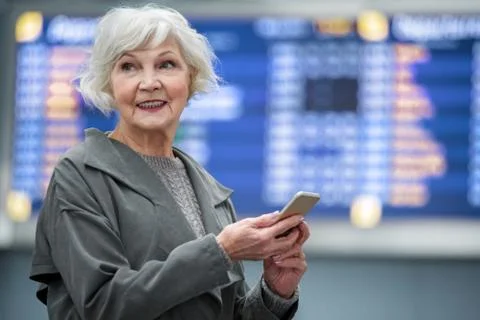 Optimistic gray-haired lady is smiling and holding smartphone Stock Photos