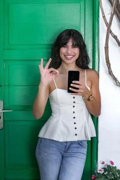 Optimistic Hispanic female with smartphone gesturing OK Stock Photos