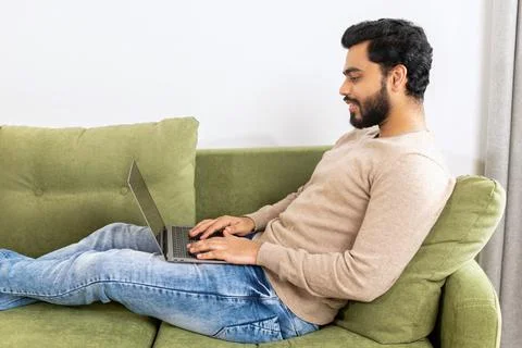Optimistic man lying on the couch and using laptop computer for messaging, happy Stock Photos