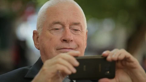 Optimistic senior man taking a selfie on his smartphone in a green street 库存影片 97006978