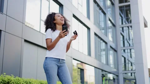 Optimistic woman in basic clothes holding smartphone and card with smile Video stock 280559957