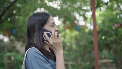 Optimistic woman looking away while talking on cell phone and standing with lush Stock Footage 252735078