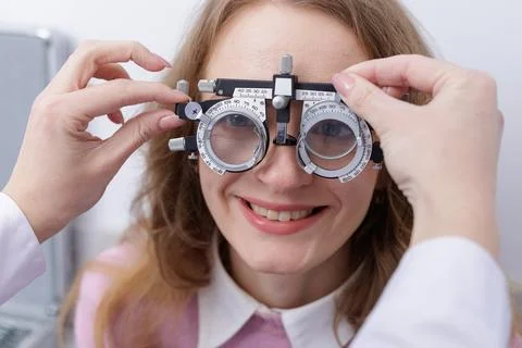 Optometrist adjusts trial frame on smiling patient during eye vision test Stock Photos