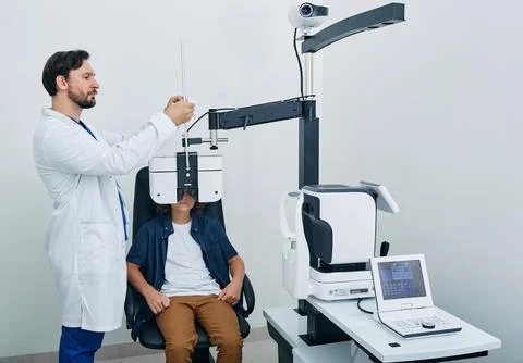 Optometrist doing vision test for curly boy patient using modern phoropter .. Stock Photos