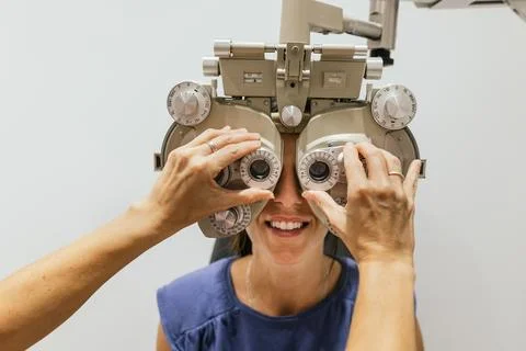 Optometrist using phoropter during eye exam for vision prescription Stock Photos