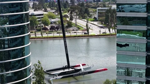 Oracle Team USA racing catamaran floats on pond between curved glass towers at 库存影片 338964483