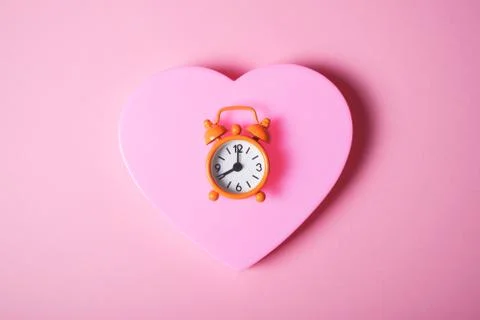 Orange alarm clock on pink heart. Stock Photos