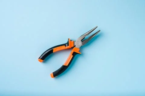 Orange and black handled needle nose pliers on a blue background Stock Photos