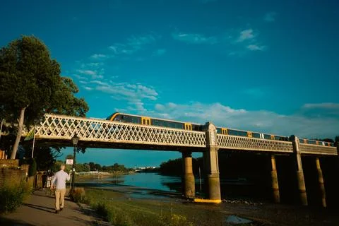 Orange and grey train crossing metal bridge over river in London Stock Photos