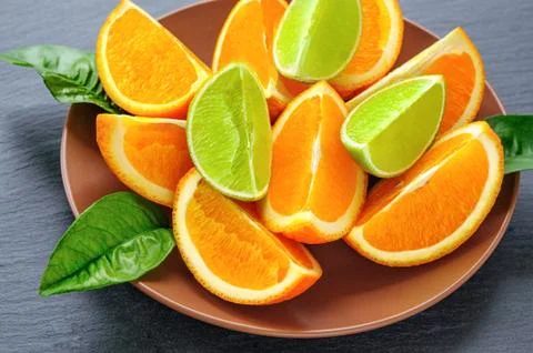 Orange and lime sliced segments  with green leaves on brown plate, black slat Stock Photos