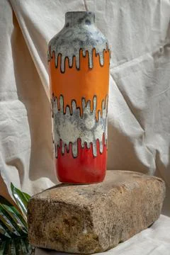 Orange and Red handmade ceramic vase on white textured table cloth. Stock Photos