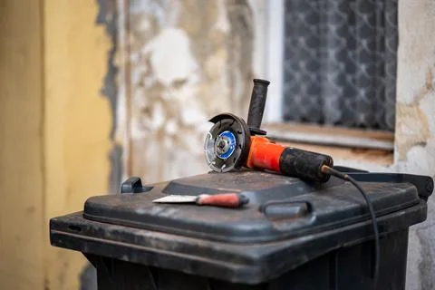 Orange angle grinder lying on a trash bin next to a spatula during renovation Foto stock