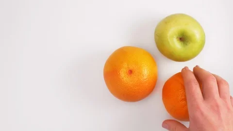 Orange, apple and grapefruit. Three fruit on a white table. Hands of women Video stock 91583497