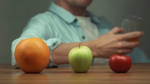 Orange, apple and tomato on table in front of man who drinking juice Stock Footage 81882239