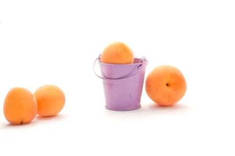 Orange apricots on a white background with a lilac bucket Stock Photos