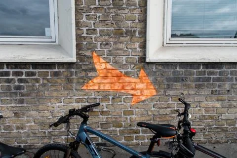 Orange arrow on the wall bettween two windows and a bike Stock Photos