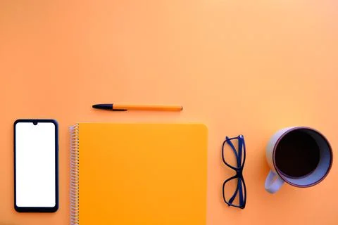 Orange background with cell phone, notebook, coffee and glasses Stock Photos