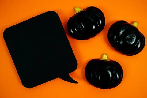 Orange background with three glossy black pumpkins and a blank black speech.. Stock Photos