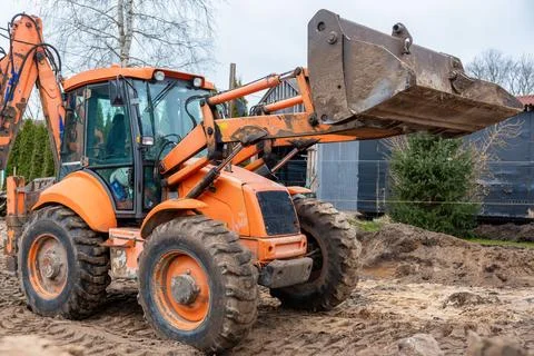 Orange Backhoe Loader on Construction Site with Raised Bucket Stock Photos
