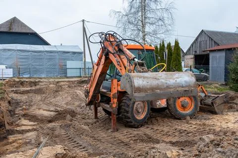 Orange Backhoe Loader at Construction Site with Rural Buildings Stock Photos