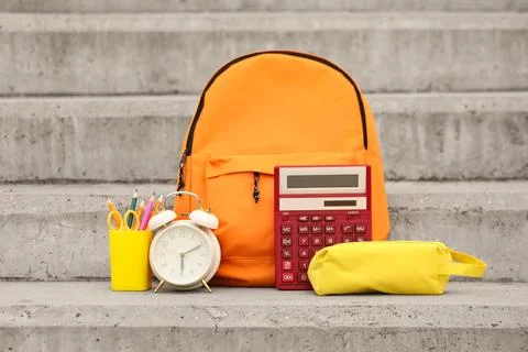 Orange backpack with school supplies including a red calculator, alarm clock, Stock Photos