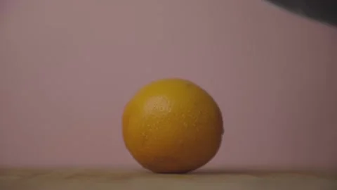 Orange Being Cut in Half by Knife against Pink Background LOG Stock Footage 136992396