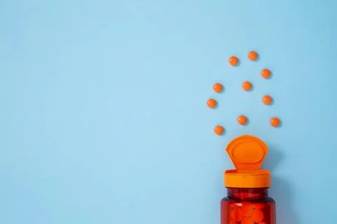 Orange bottle container with medication tablets and capsules on blue backgrou Stock Photos