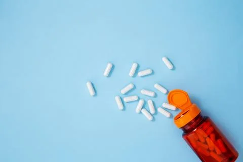 Orange bottle container with various white medication tablets and capsules on Stock Photos