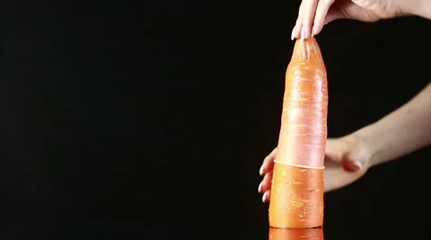 Orange carrot with a condom on a black background Stock Footage 62478920