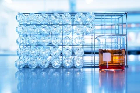 Orange chemical solution in science beaker and glass test tube in metal rack Stock Photos