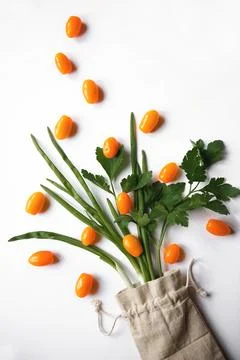 Orange cherry tomatoes flat lay with parsley greens in a cloth bag on a whi.. Stock Photos