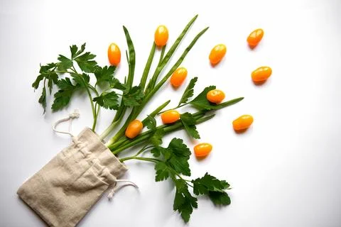 Orange cherry tomatoes flat lay with parsley greens in a cloth bag on a whi.. Stock Photos