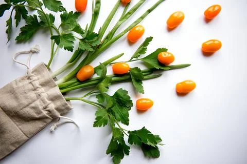 Orange cherry tomatoes flat lay with parsley greens in a cloth bag on a whi.. Stock Photos