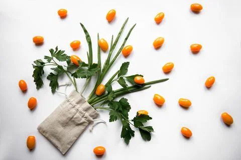 Orange cherry tomatoes flat lay with parsley greens in a cloth bag on a whi.. Stock Photos