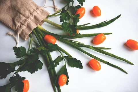 Orange cherry tomatoes flat lay with parsley greens in a cloth bag on a whi.. Stock Photos