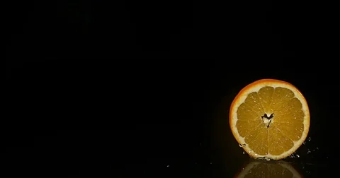 Orange, citrus sinensis, Slice rolling on Water against Black Background, Slow Stock Footage 75971966